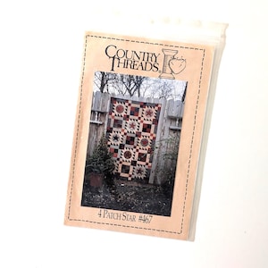 May include: A package for a quilt pattern titled "Country Threads 4 Patch Star #467." The pattern features a quilt with red, brown, and cream star and square designs. The package is in a clear plastic sleeve.