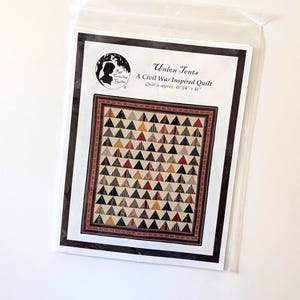 May include: A Civil War-inspired quilt pattern titled "Union Tents" in a clear plastic sleeve. The quilt design features rows of small, colorful triangles in shades of brown, red, and tan. The quilt measures approximately 40 3/4" x 46".