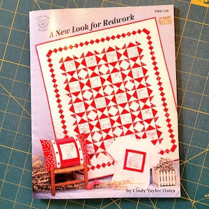 May include: A red and white quilt pattern with a redwork design. The quilt pattern is called "A New Look for Redwork" and is by Cindy Taylor Oates. The pattern is for sale for $12.50.