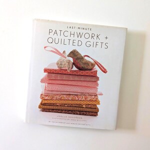May include: A hardcover book titled Last-Minute Patchwork + Quilted Gifts by Joelle Hoverson. The cover features a stack of folded fabric squares in shades of pink, orange, and brown, topped with two small, stuffed fabric bird ornaments with loops.