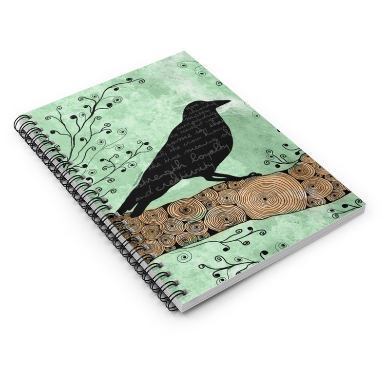 May include: Spiral-bound notebook with a raven silhouette on a branch. The cover has a light green watercolour background, black floral accents, and text. The raven is black with white text inside.