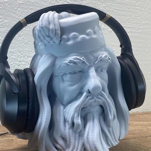 May include: A light blue bust of a bearded man wearing black headphones. The bust has detailed facial features and a hat. The headphones are over-ear style with black earcups and a black headband.