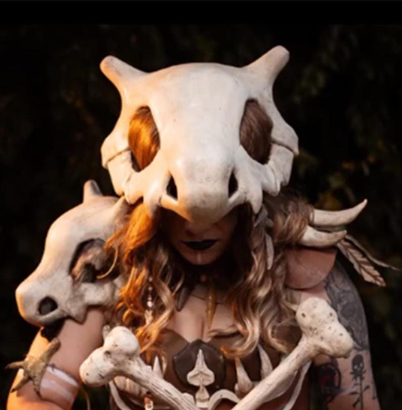 Puede incluir: Un detallado disfraz de cosplay con un casco de calavera con forma de hueso y una armadura para los hombros. El disfraz incluye detalles de hueso en el pecho y los brazos, con una combinaci&oacute;n de colores marr&oacute;n y beige. El pelo de la persona es visible debajo del casco.