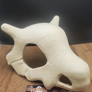 Puede incluir: Una m&aacute;scara en forma de hueso de color crema con cuencas oculares grandes y dos protuberancias en forma de cuerno. La m&aacute;scara tiene una superficie texturizada y probablemente est&aacute; hecha de un material r&iacute;gido. La m&aacute;scara est&aacute; dise&ntilde;ada para ser usada, con un recorte para la boca.