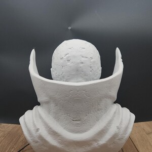 Puede incluir: Un busto blanco de un personaje con cabeza redondeada y cuello tipo capa. El busto est&aacute; sobre un fondo negro y sobre una base negra. Se ve una tarjeta de visita con el texto "Mr. Rabbit Trinkets".