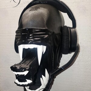 Może przedstawiać: Czarno-biała dekoracja ścienna z motywem Obcego ze słuchawkami. Rzeźba przedstawia głowę obcego z dużymi białymi zębami i opaską na oczy. Widoczny jest tekst "Xenowares" i "Game Over Man".