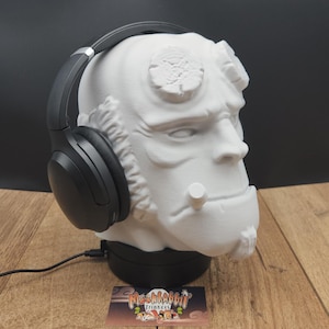 May include: A white bust of a character with black headphones resting on its head. The bust is on a black base, and a business card with the text "Miss Rabbit Trinkets" is in front. The background is black, and the surface is wood.