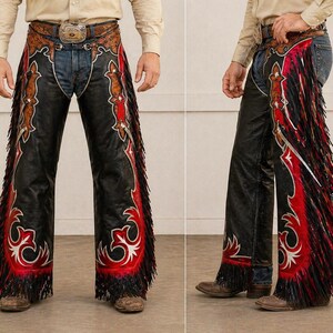 May include: Black leather chaps with red and white decorative accents and long fringe. The chaps feature a detailed design along the sides and bottom, with a brown leather belt and buckle.