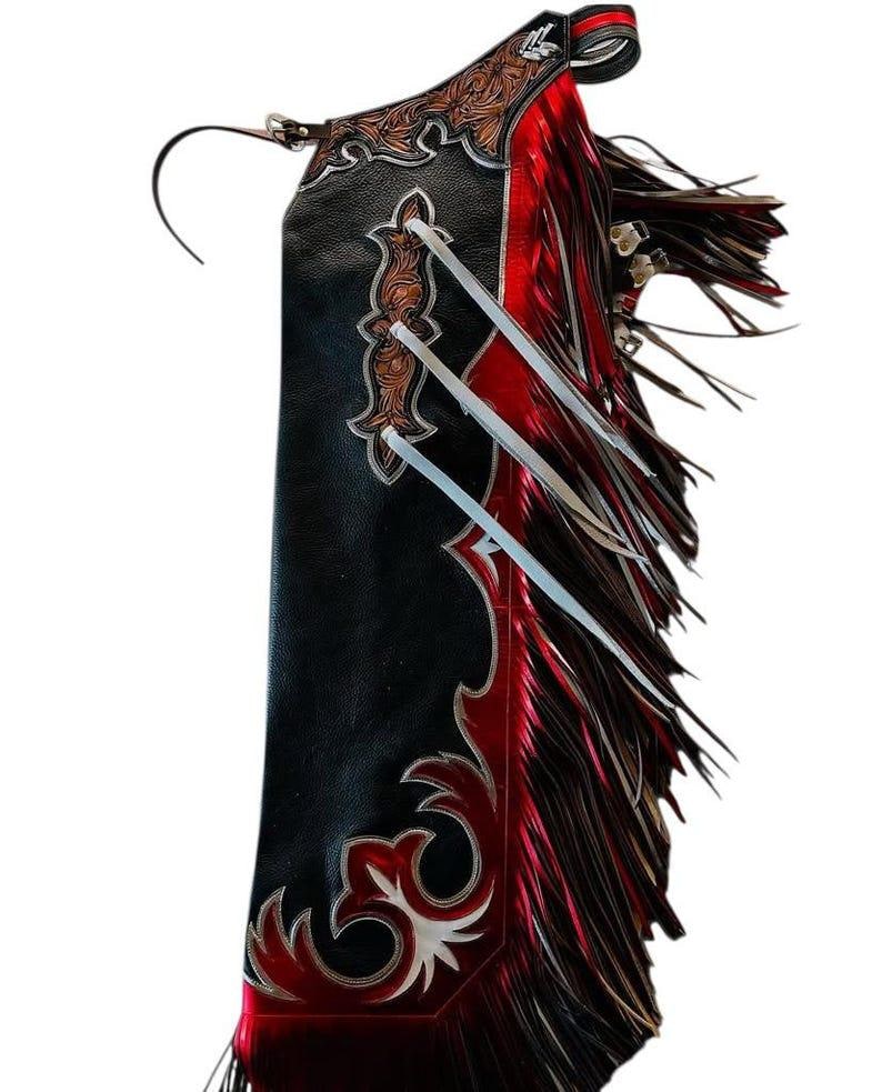 May include: Black and red leather chaps with decorative silver and brown accents. The chaps feature a fringe along the side and decorative stitching. A western-style garment.
