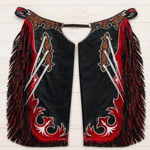 May include: Black leather chaps with red and white decorative accents. The chaps feature a red fringe along the sides and decorative silver-colored embellishments. The top portion has brown leather detailing.