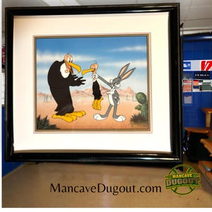 Puede incluir: Una ilustración de dibujos animados enmarcada de Bugs Bunny sosteniendo un buitre de dibujos animados por el cuello. El buitre tiene una expresión de sorpresa. El fondo es una escena de desierto con un cactus.