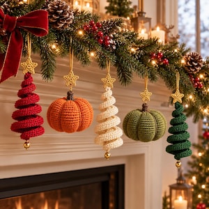 Könnte beinhalten: Fünf gehäkelte Ornamente hängen an einer Girlande, darunter drei spiralförmige Bäume in Rot, Creme und Grün sowie zwei runde Kürbisse in Orange und Olivgrün. Jedes Ornament hat einen kleinen gelben gehäkelten Stern und eine goldene Perle.