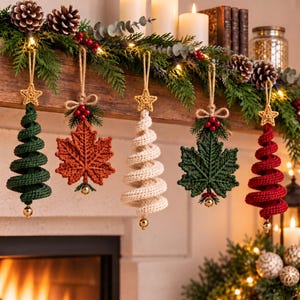 May include: Five hanging ornaments featuring three spiral crochet Christmas trees in green, cream, and red, and two crochet maple leaves in orange and dark green. Each ornament is topped with a small crocheted star and a gold bead at the base.