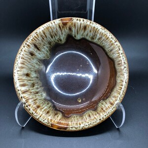 May include: A brown and white glazed ceramic bowl with a wavy rim. The bowl has a dark brown interior and a light brown exterior with white streaks.