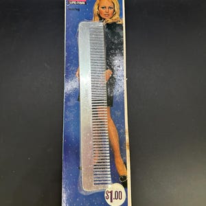 May include: A silver aluminum comb with the words "LIFE-TIME teasing" printed on the handle. The comb is packaged on a blue and white card with a woman's image and the text "ALUMINUM" and "$1.00". The card also includes the text "LIFETIME COMB CO., Boston, Mass."