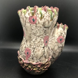 May include: A ceramic vase with a unique, organic shape and a textured, white glaze. The vase is decorated with pink and green accents and has a ruffled rim.