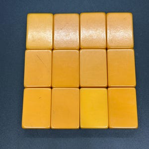 May include: A collection of twelve rectangular, amber-colored tiles arranged in a grid. The tiles have rounded corners and a smooth, glossy surface. The color varies slightly across the tiles, ranging from light yellow to a deeper amber.