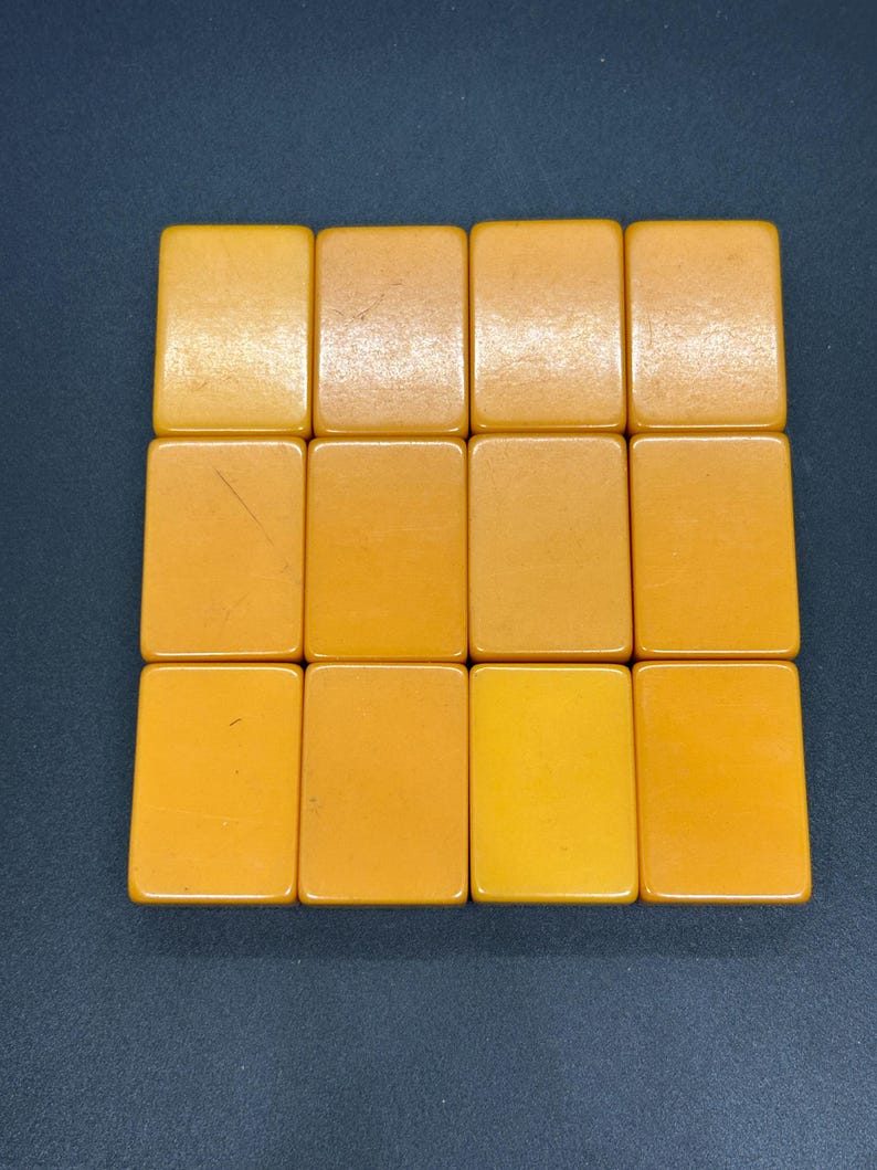 May include: A collection of twelve rectangular, amber-colored tiles arranged in a grid. The tiles have rounded corners and a smooth, glossy surface. The color varies slightly across the tiles, ranging from light yellow to a deeper amber.