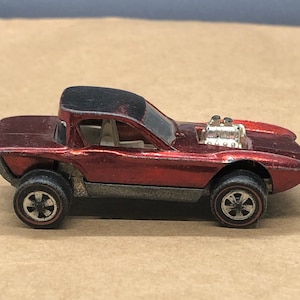 May include: Red Hot Wheels toy car with a black roof and exposed engine. The car has a detailed interior and black wheels.