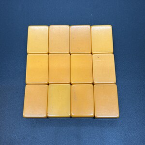 May include: Twelve amber-coloured rectangular tiles arranged in a grid formation. The tiles have a smooth, glossy surface and are set against a dark blue background. The tiles appear to be made of a solid material.