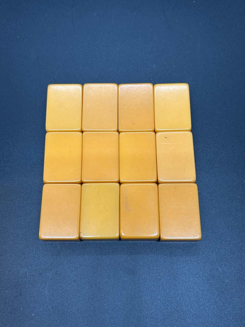 May include: Twelve amber-coloured rectangular tiles arranged in a grid formation. The tiles have a smooth, glossy surface and are set against a dark blue background. The tiles appear to be made of a solid material.