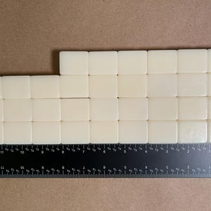 May include: A set of twenty-three off-white rectangular tiles arranged in three rows, positioned against a black ruler showing measurements in inches. The tiles are smooth and uniform in color, with the ruler indicating a width of 12 inches.