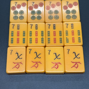 May include: Twelve rectangular Mahjong tiles in a light yellow hue. The tiles feature red, green, and black symbols. The tiles are arranged in three rows of four.