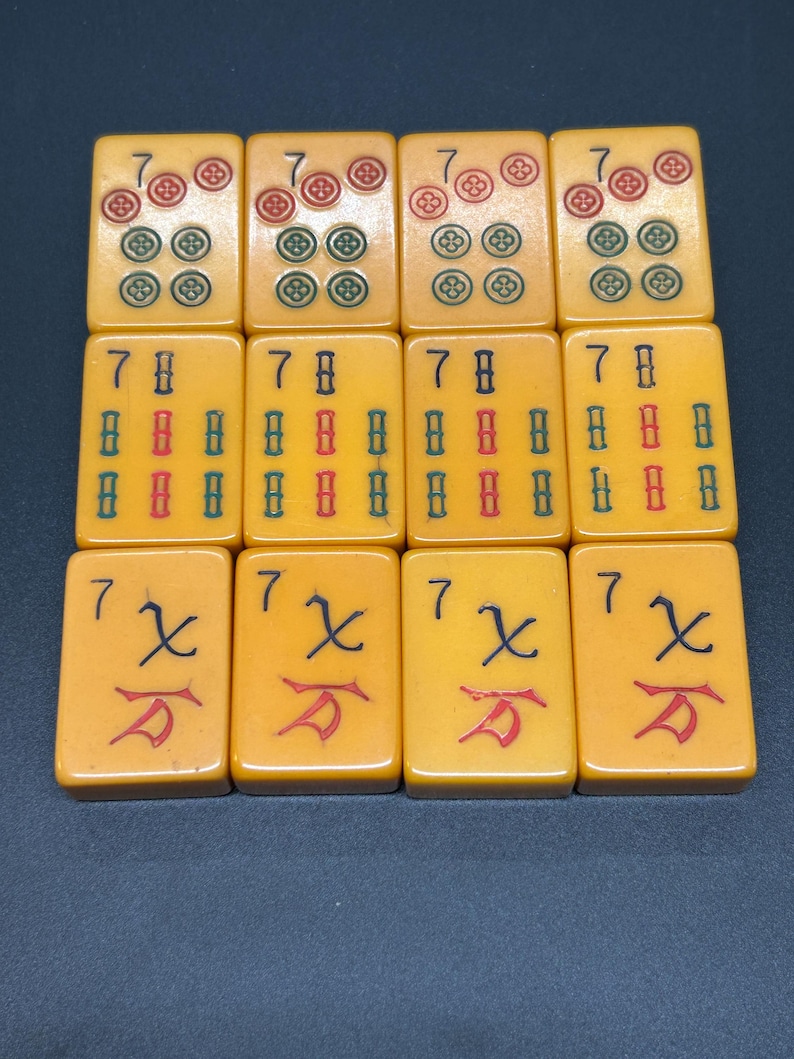 May include: Twelve rectangular Mahjong tiles in a light yellow hue. The tiles feature red, green, and black symbols. The tiles are arranged in three rows of four.