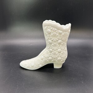 May include: White milk glass boot shaped vase with a raised floral pattern.