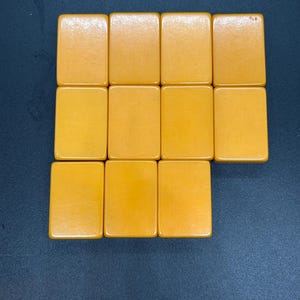 May include: A collection of twelve rectangular, amber-colored tiles arranged on a dark blue surface. The tiles are smooth and have rounded corners, suggesting they are game pieces.