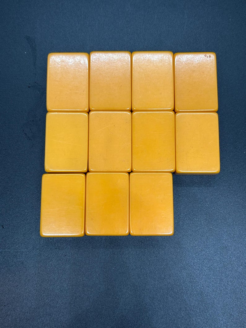 May include: A collection of twelve rectangular, amber-colored tiles arranged on a dark blue surface. The tiles are smooth and have rounded corners, suggesting they are game pieces.