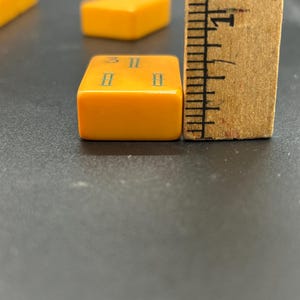 May include: Close-up of a vintage orange Mahjong tile with the number 3 and two 8s in blue. A wooden ruler is next to the tile. Other orange tiles are in the background.