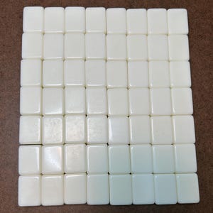 May include: A grid of forty-nine blank, rectangular, off-white tiles arranged in seven rows and seven columns. Each tile has a smooth, uniform surface with rounded corners, creating a consistent, repetitive pattern across the entire square formation.