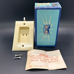 May include: A vintage white electrical outlet with a box and screws. The box is blue with a white eagle logo and the text "EAGLE ELECTRIC" and "714 ONE UL". The box also has a notice that reads "NOTICE USE ONLY COPPER OR COPPER CLAD WIRE WITH THIS DEVICE NO. 1301T-MUL".