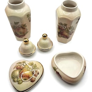 May include: A collection of vintage ceramic decorative items. The set includes two vases, two small lidded jars, and two heart-shaped dishes. Each piece features a cream-colored base with a fruit design and gold trim.