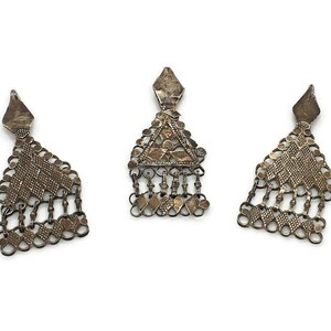 May include: Three silver filigree pendant charms with intricate designs. Each charm features a diamond-shaped top and a cascading fringe of smaller, interconnected shapes.