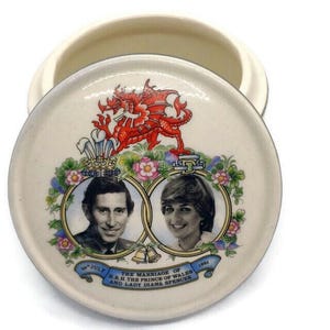 May include: A white ceramic trinket box with a red dragon and floral design. The lid features a photo of Prince Charles and Lady Diana Spencer with the text "The Marriage of H.R.H. The Prince of Wales and Lady Diana Spencer 29th July 1981".