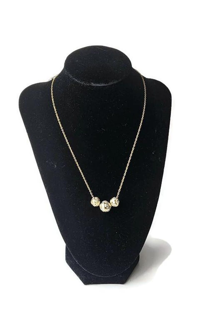 May include: A gold-colored necklace with three textured spherical pendants. The necklace is displayed on a black velvet bust against a white background. The chain is delicate and the pendants have a woven design.
