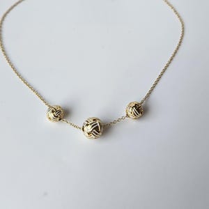May include: A delicate gold necklace featuring three textured, spherical pendants. The pendants are evenly spaced along the fine chain, creating a balanced and elegant design. The necklace is set against a plain white background.