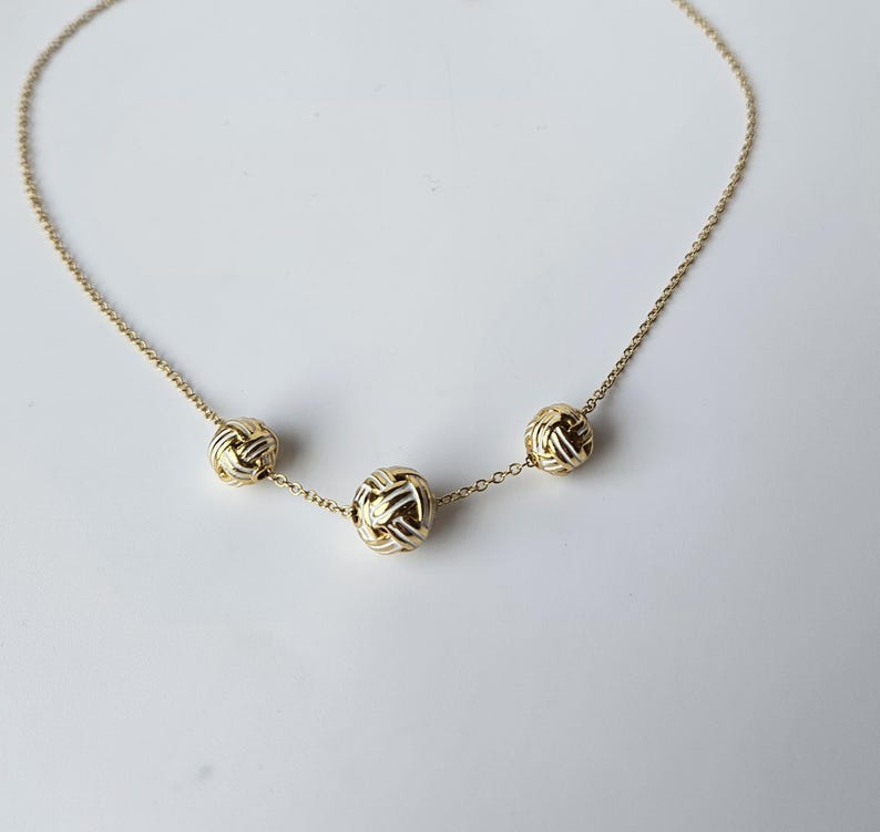 May include: A delicate gold necklace featuring three textured, spherical pendants. The pendants are evenly spaced along the fine chain, creating a balanced and elegant design. The necklace is set against a plain white background.