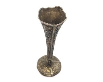 May include: A silver vase with an ornate design. The vase is tall and slender with a flared top and a round base.