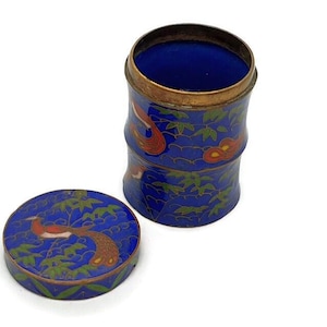 Puede incluir: Una caja de baratijas de cloisonné azul y dorado con tapa. La caja está decorada con pájaros y flores rojos y dorados. La tapa está decorada con un pájaro rojo y dorado.