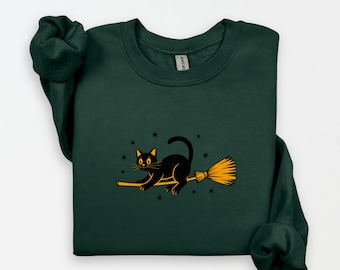 Puede incluir: Sudadera verde oscuro con un gato negro montado en una escoba naranja. El gato tiene ojos amarillos y está rodeado de estrellas. Un diseño con temática de Halloween, perfecto para la temporada.