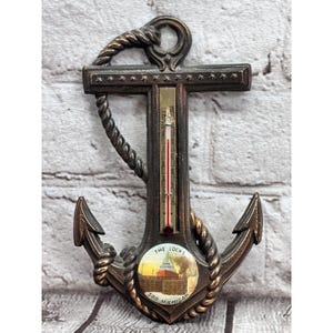 May include: Bronze-colored anchor-shaped thermometer with a rope design. The thermometer has a red liquid column and a small circular image of a building with the text "THE LOCKS SOO MICHIGAN".