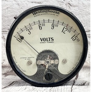 May include: Vintage Westinghouse voltmeter with a black bezel and a cream-colored face. The gauge reads "VOLTS DIRECT CURRENT" and features a needle pointing to zero. The text "Westinghouse Electric & Manufacturing Co." is visible at the top.