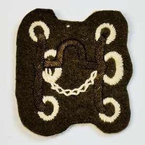 May include: A dark green felt patch with a white embroidered design. The design features a stylized letter "H" surrounded by four circles.
