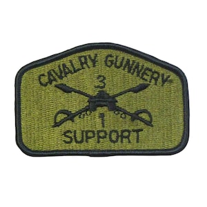 May include: A green embroidered patch with black stitching. The patch features the text "Cavalry Gunnery 3 1 Support". A black silhouette of a helicopter with crossed sabers is in the center of the patch.