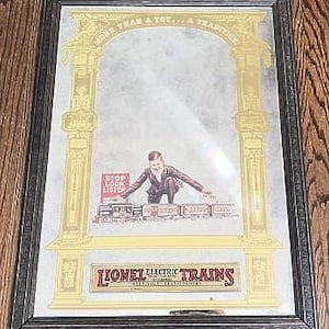 May include: Framed vintage Lionel Electric Trains advertisement. The artwork features a man with a train set, framed by ornate gold columns and the text "MORE THAN A TOY... A TRADITION!" and "STOP LOOK LISTEN".