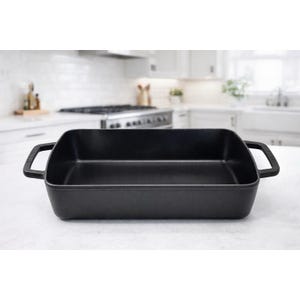May include: A black rectangular cast iron baking dish with two handles. The dish is empty and sits on a white countertop. The background shows a kitchen with white cabinets and appliances.