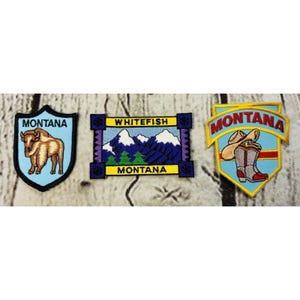 May include: Three embroidered patches with Montana themes. One features a bison, another depicts mountains and the text "Whitefish Montana", and the third shows a cowboy hat and boots. Each patch has a different shape and color scheme.
